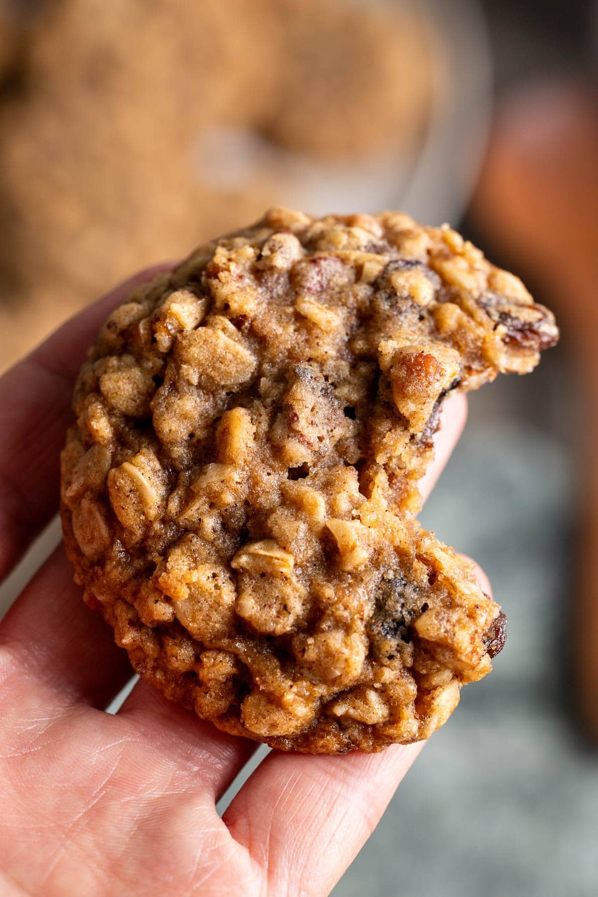 A hand holding a brown butter oatmeal raisin cookie with a bite taken out of it to show the chewy texture.