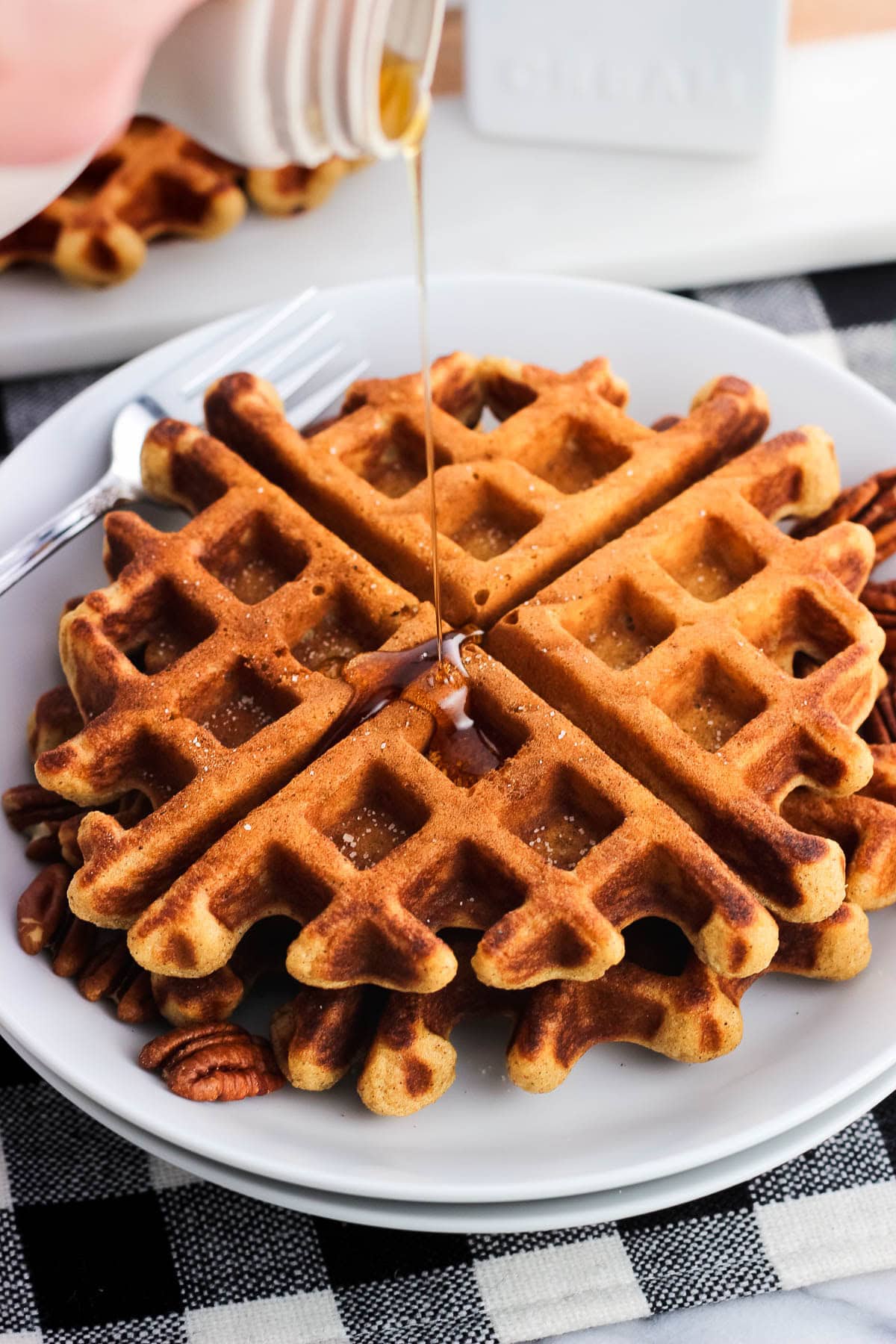 Maple syrup being drizzled onto two gingerbread waffles on a plate.