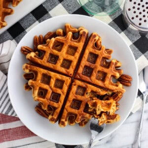 Gingerbread waffles on a plate served with pecan halves and maple syrup.
