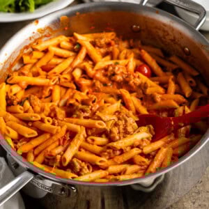 A pan of penne alla vodka with sausage and tomatoes in a large pan with a serving spoon.