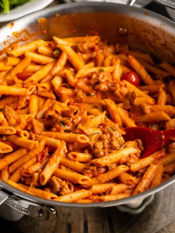 A pan of penne alla vodka with sausage and tomatoes in a large pan with a serving spoon.