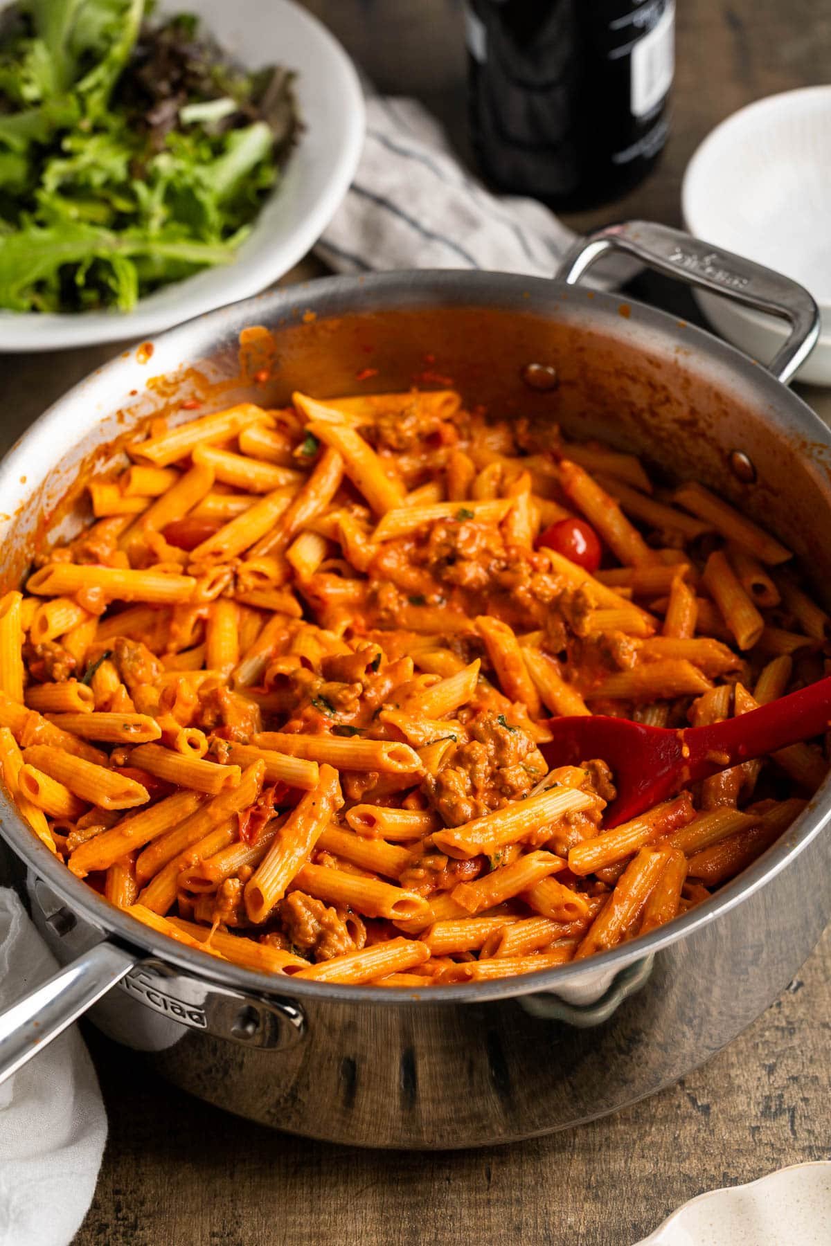 A pan of penne alla vodka with sausage and cherry tomatoes in a large pan with a serving spoon.
