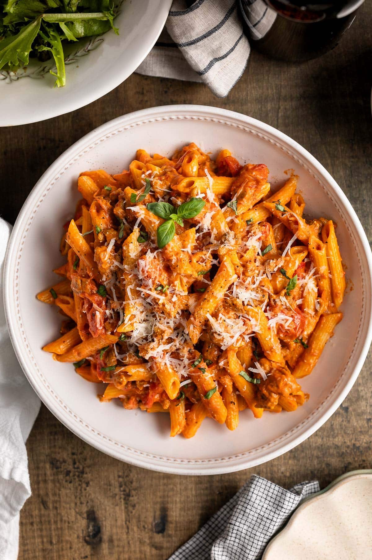 A big bowl of sausage vodka pasta garnished with fresh basil and grated Pecorino Romano.