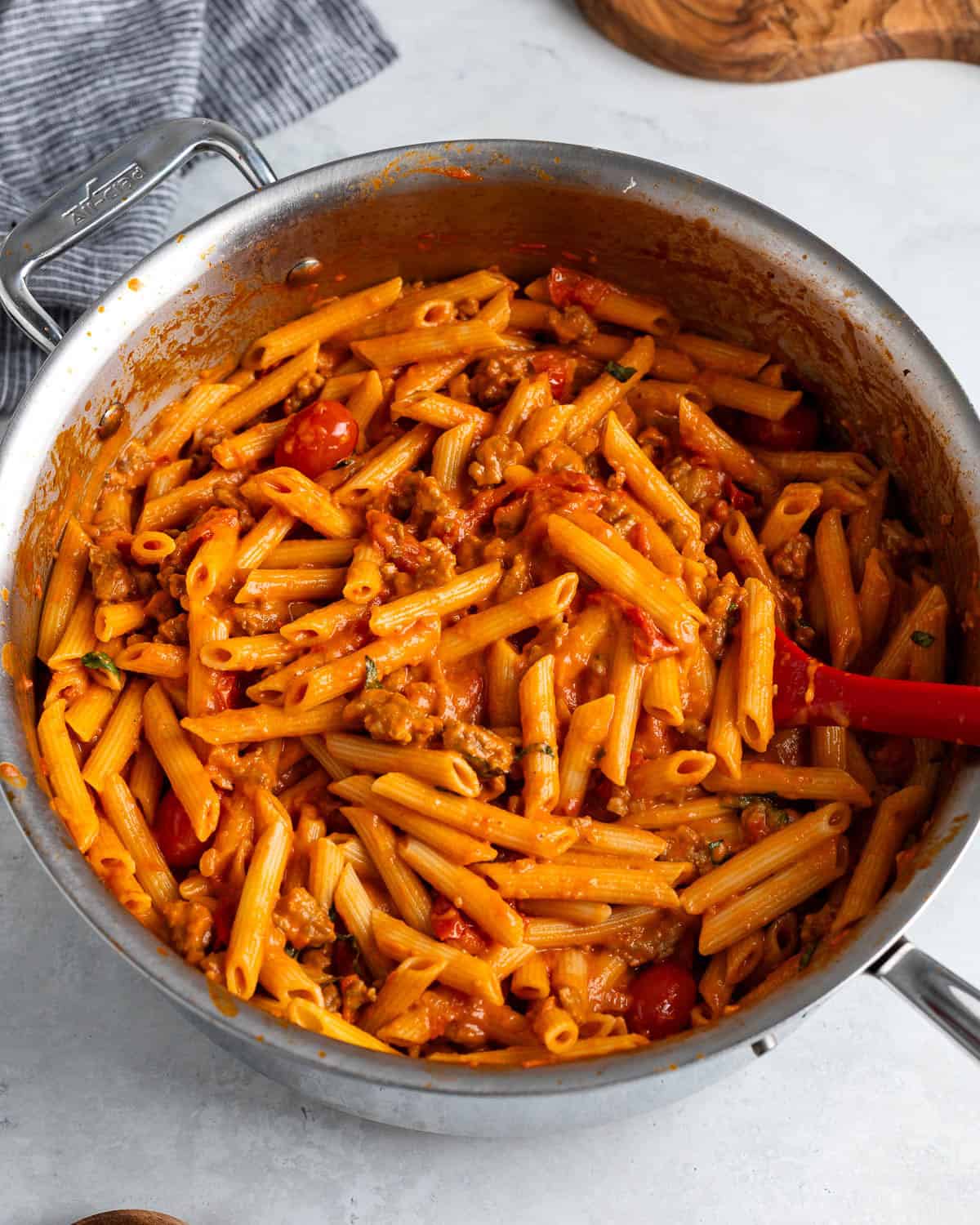 Cooked penne stirred into the pan with the sauce with basil.