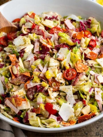 A large Italian sub salad in a serving bowl with serving spoon.