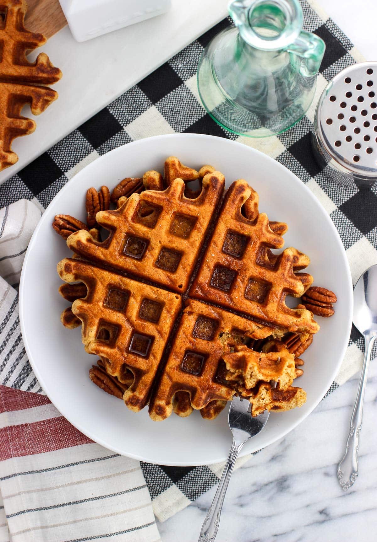 Gingerbread waffles on a plate served with pecan halves and maple syrup.