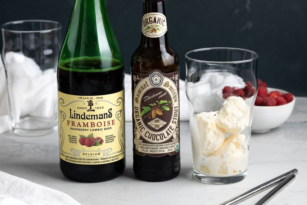 A bottle of raspberry lambic, a bottle of chocolate stout, and vanilla ice cream in a large glass.