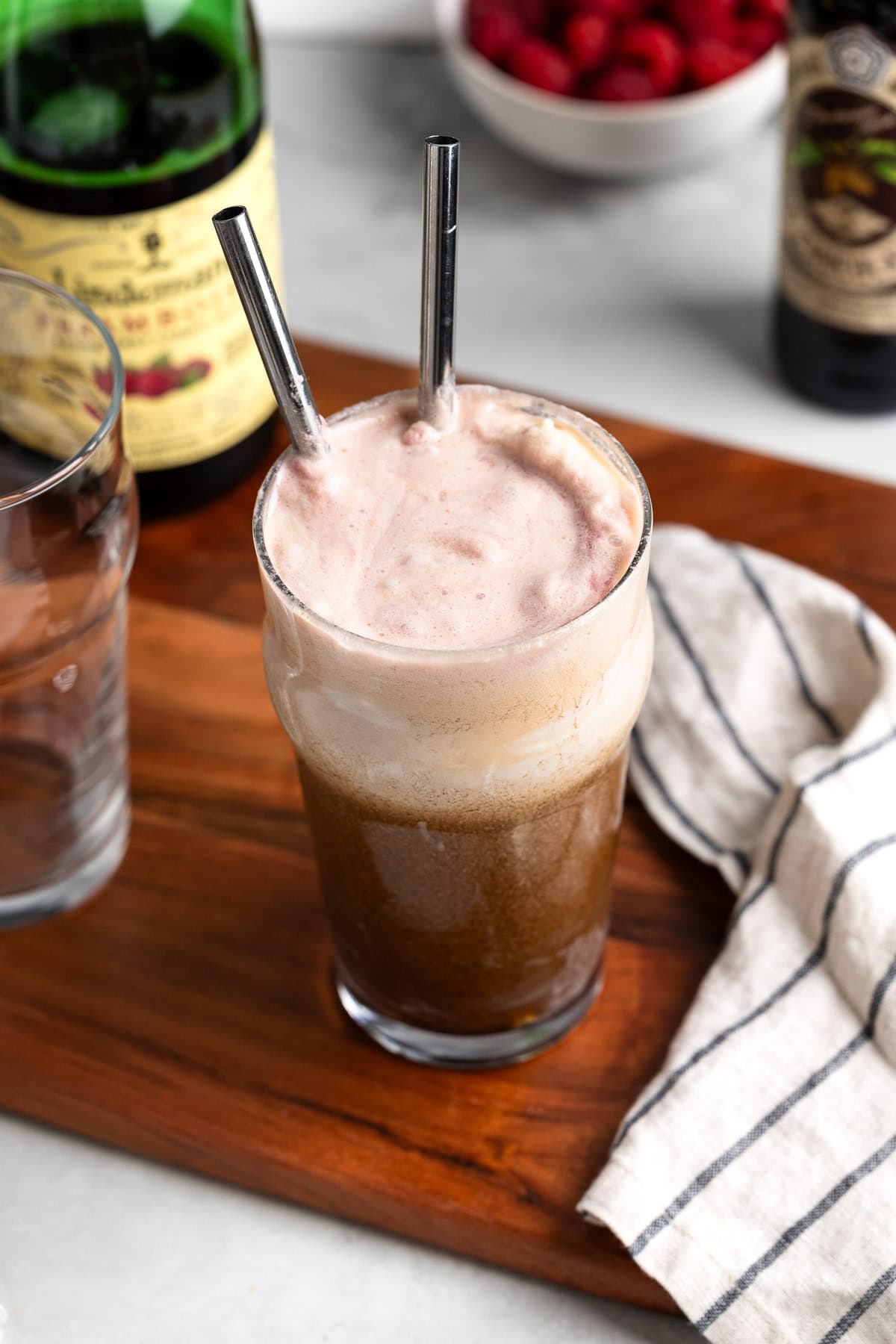 A raspberry beer float stirred together in a glass with two metal straws.