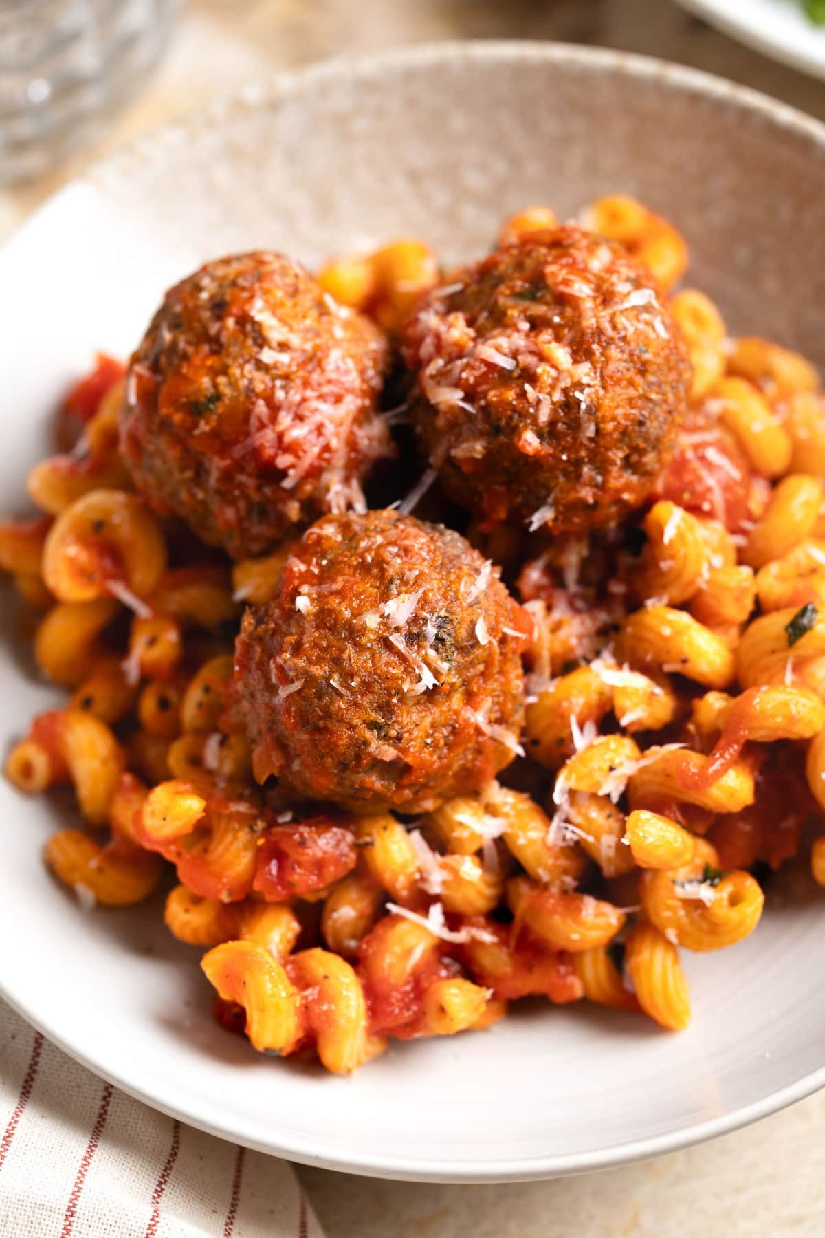 A dinner plate of three turkey meatballs and curly macaroni with red sauce.