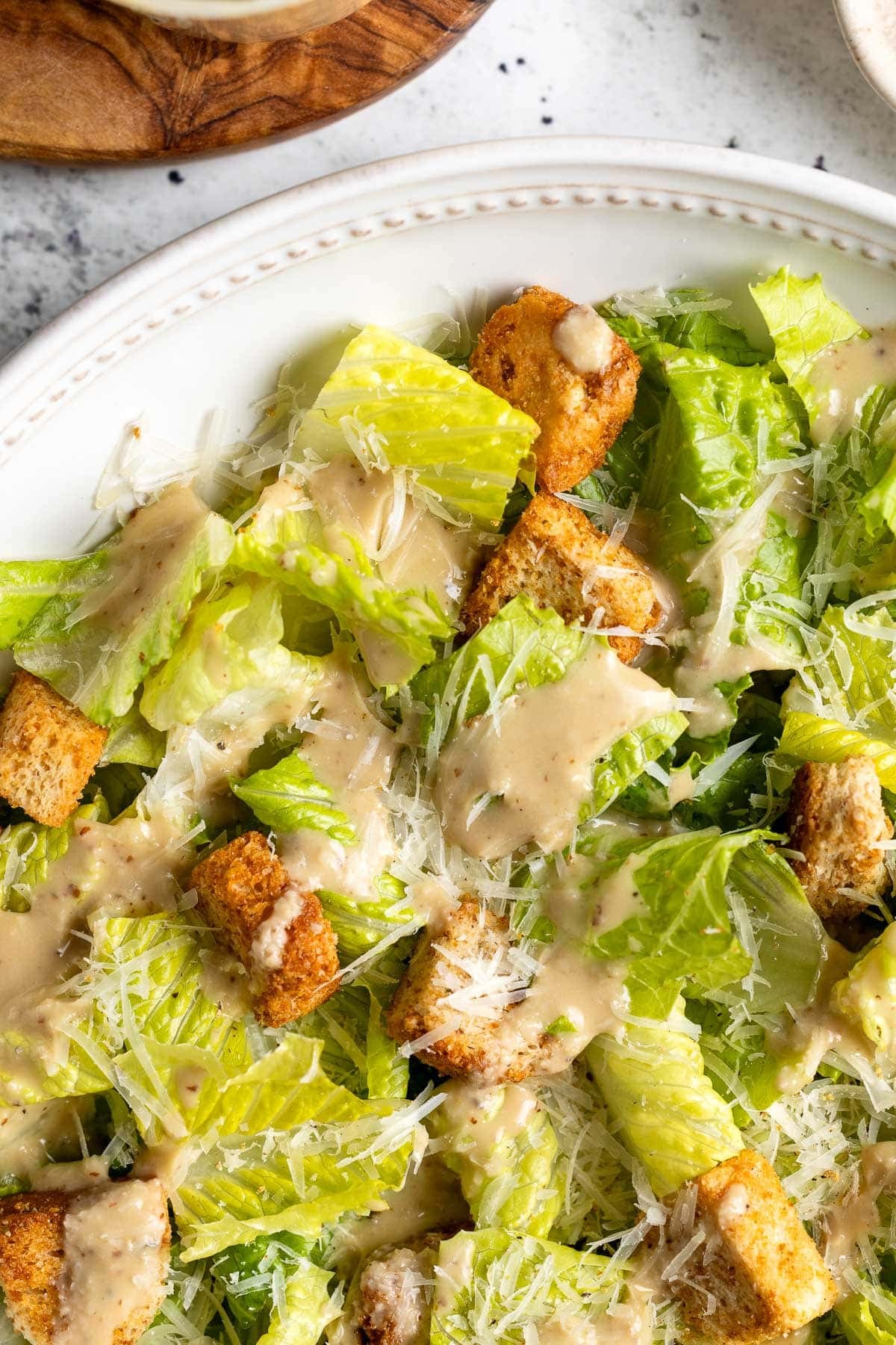 Creamy Caesar vinaigrette dressing a salad with grated Parmesan and croutons.