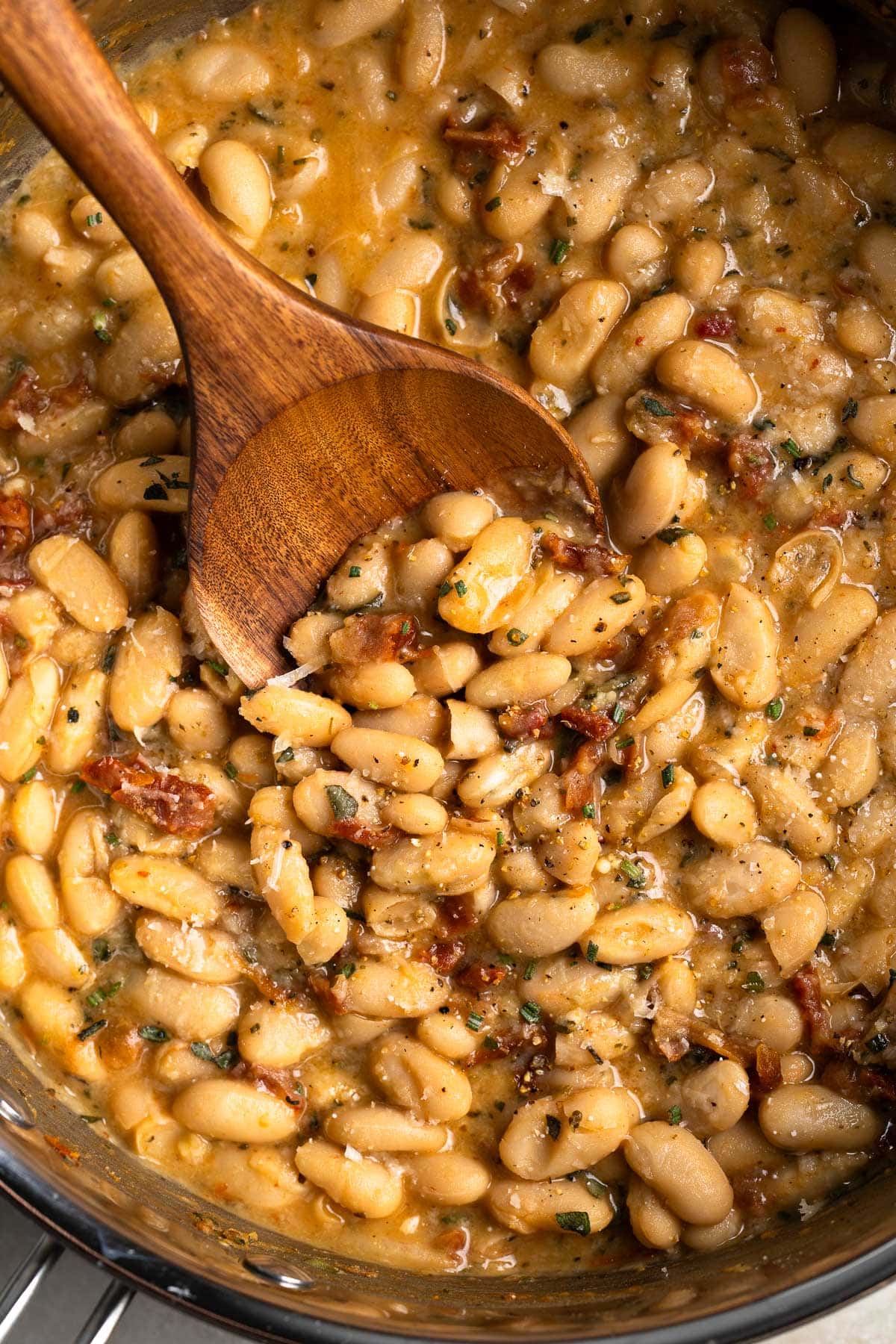 Tuscan-style creamy white beans in a pan with a wooden spoon.