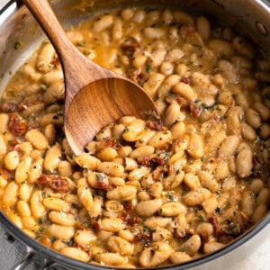 A wooden serving spoon being dipped into a pan of Tuscan white beans.