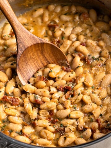 A wooden serving spoon being dipped into a pan of Tuscan white beans.