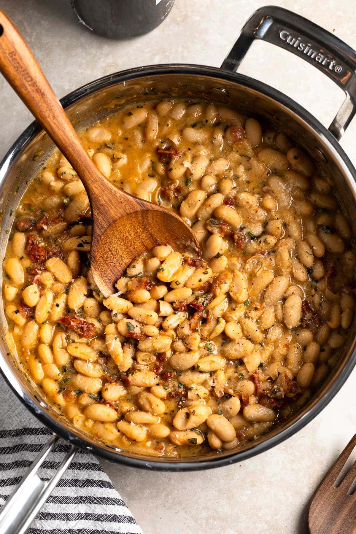 A wooden serving spoon being dipped into a pan of Tuscan white beans.