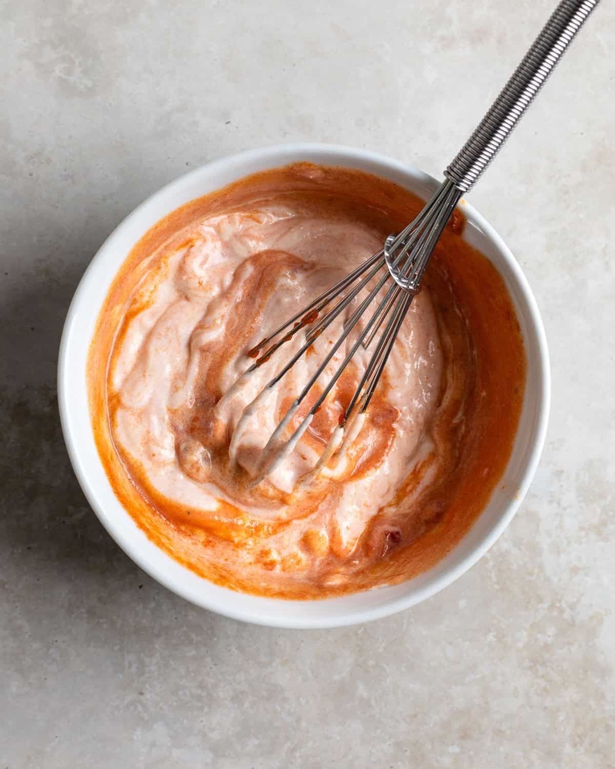 Yogurt being whisked together with hot sauce in a smaller bowl.