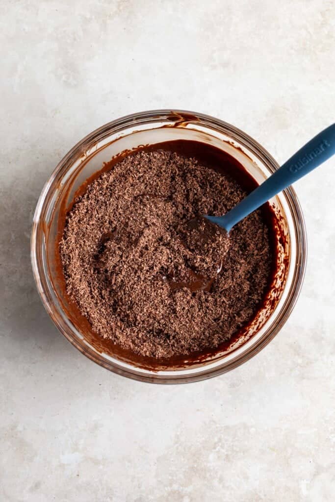 Grated chocolate poured into a bowl of melted chocolate.