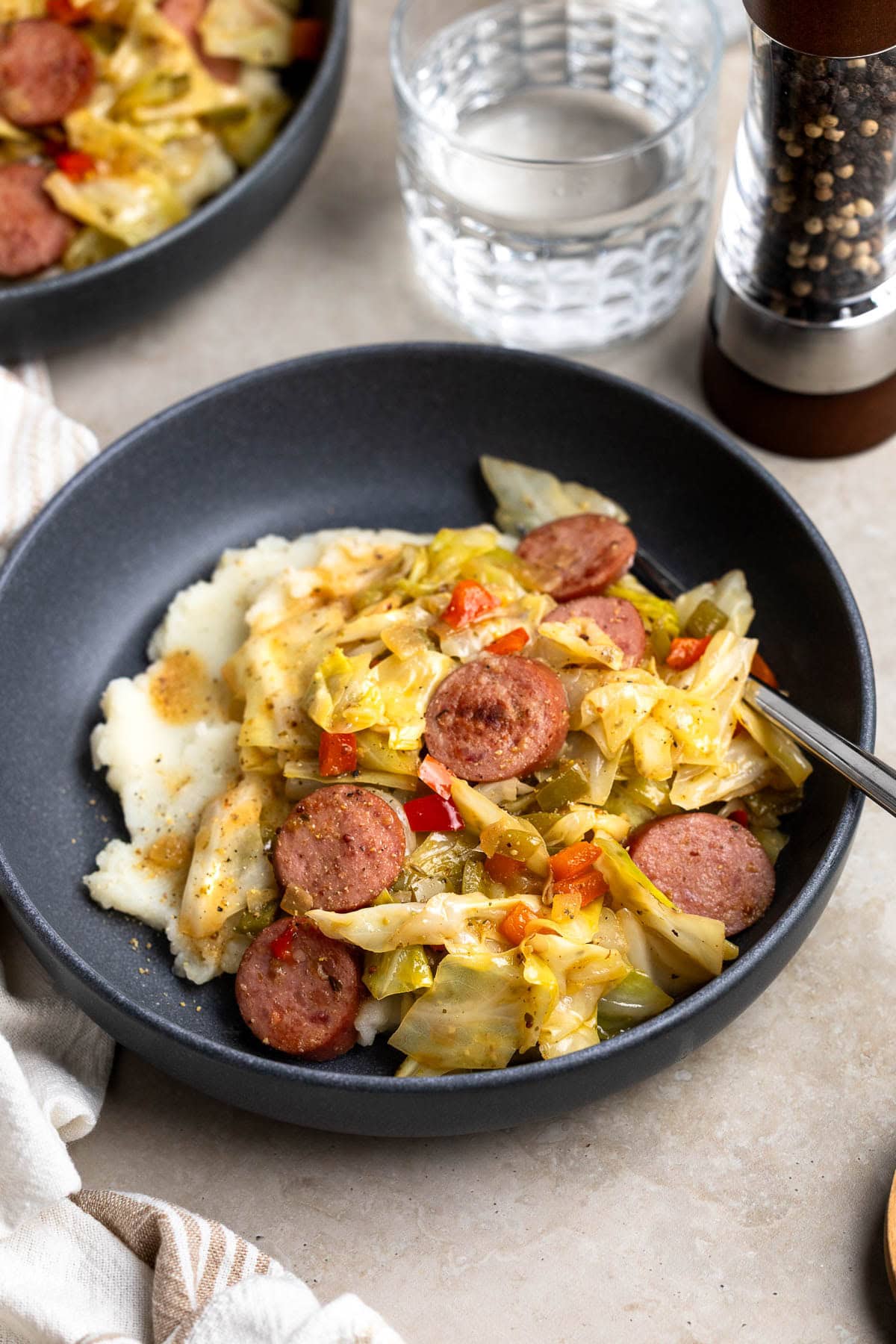 A serving of fried cabbage and sausage over mashed potatoes in a shallow bowl.