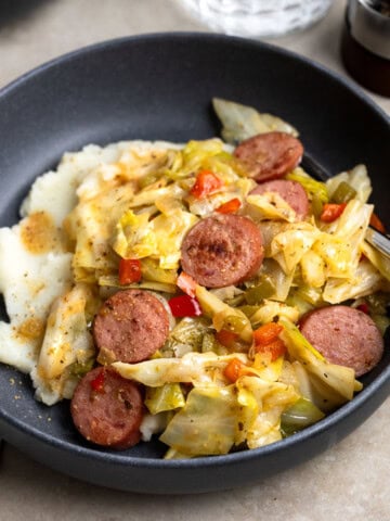 A serving of fried cabbage and sausage over mashed potatoes in a shallow bowl.