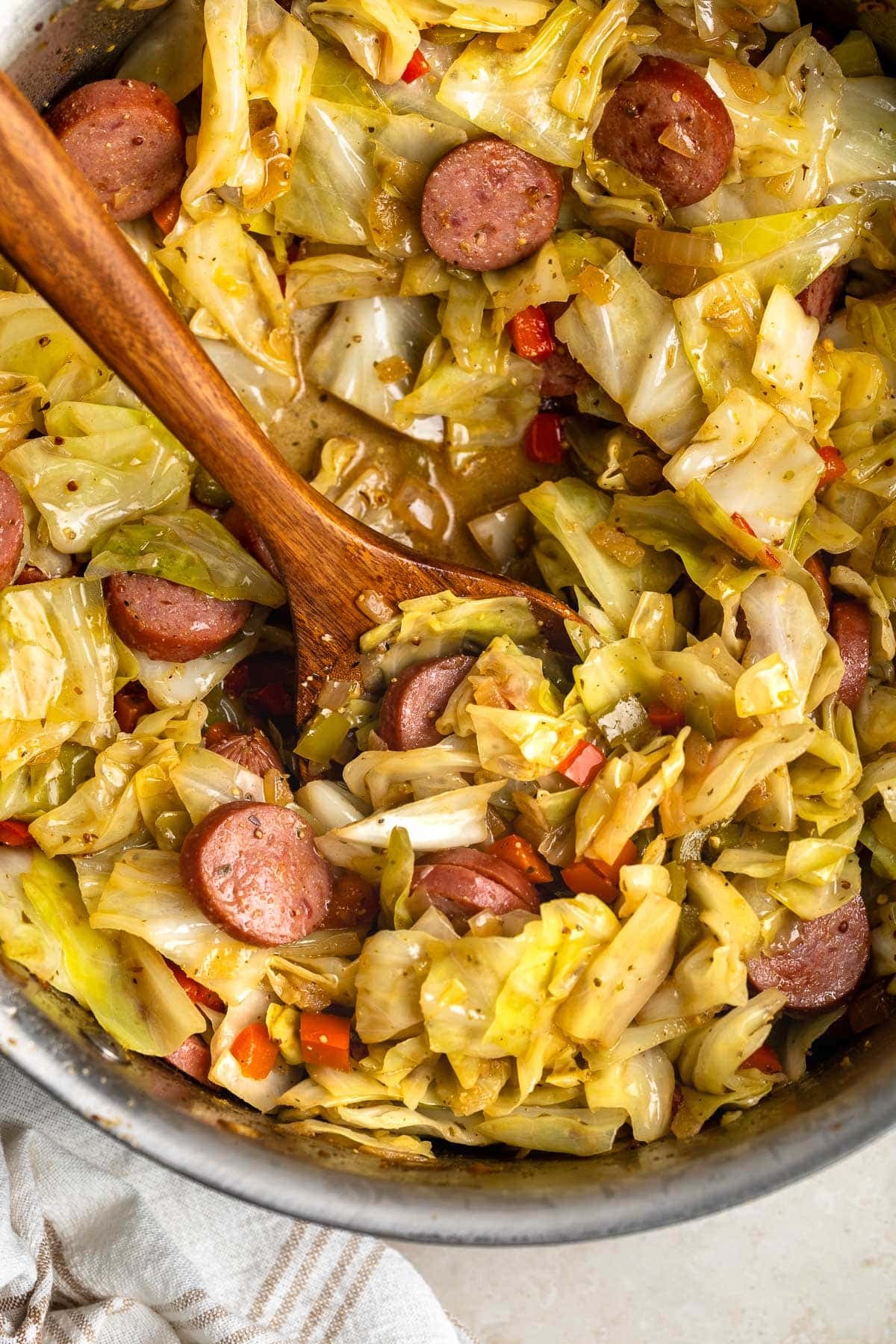 A wooden serving spoon in a skillet of fried cabbage ready to serve.