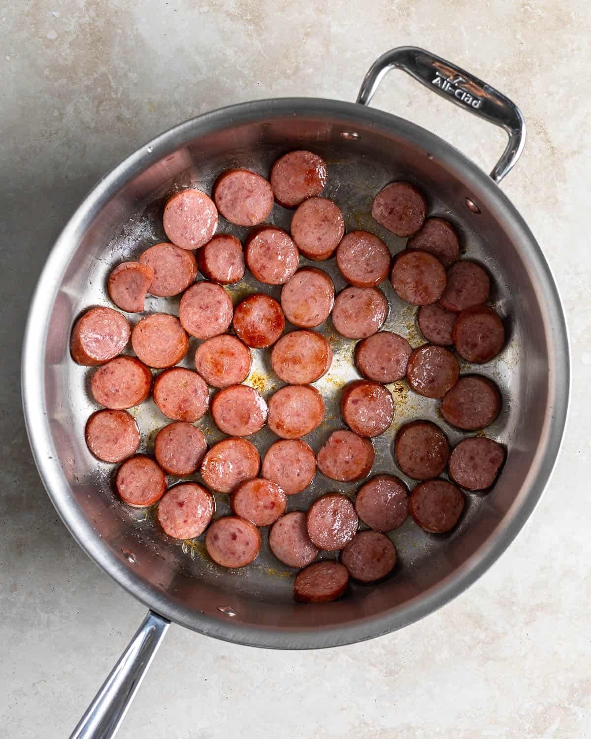 Smoked sausage rounds browning in a pan.