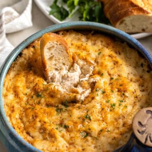 A piece of bread dunked into baked crab dip showing the creamy consistency underneath the melted cheese topping.
