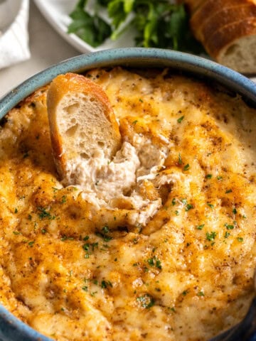 A piece of bread dunked into baked crab dip showing the creamy consistency underneath the melted cheese topping.