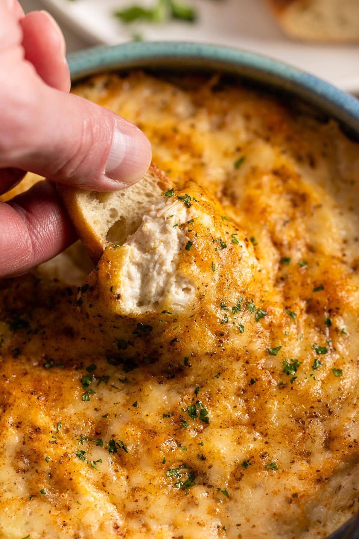 A hand dipping a baguette slice into a bowl of hot crab dip.