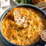 A piece of bread dunked into baked crab dip showing the creamy consistency underneath the melted cheese topping.