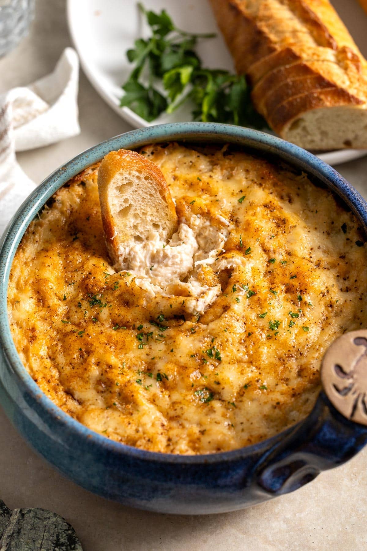 A piece of bread dunked into baked crab dip showing the creamy consistency underneath the melted cheese topping.