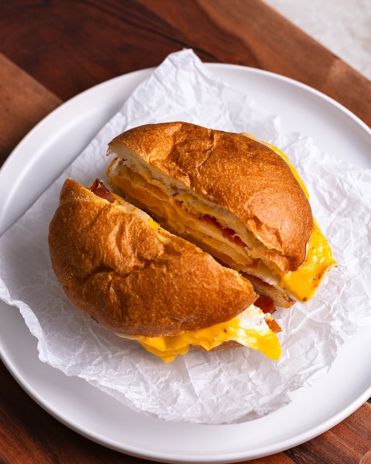 A Taylor ham egg and cheese sandwich sliced in half on a sheet of parchment paper.