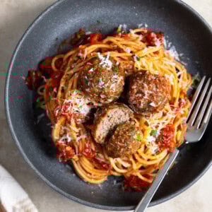 A plate of spaghetti and beef meatballs with a fork.
