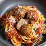 Meatballs on top of a plate of spaghetti with one meatball cut in half.
