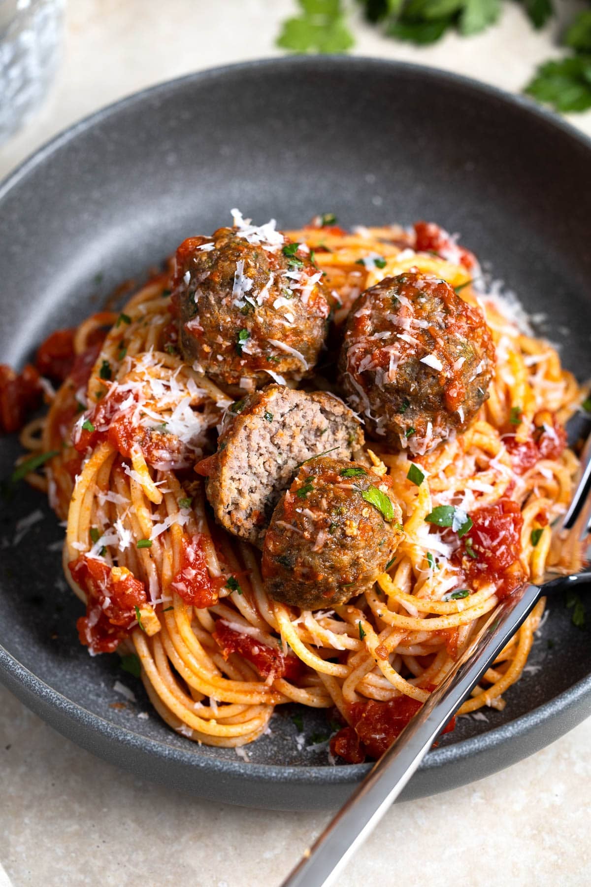 Meatballs on top of a plate of spaghetti with one meatball cut in half.