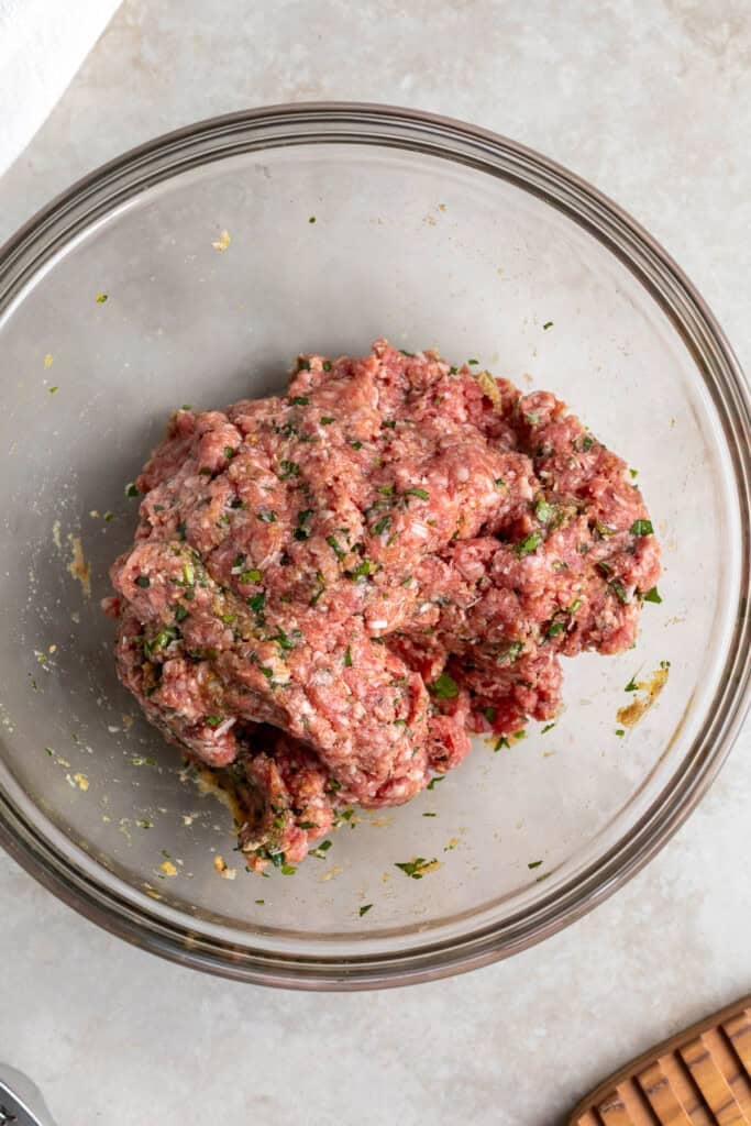 The combined beef meatball mixture in a large glass mixing bowl.