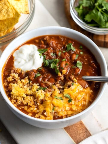 A bowl of turkey chili made in the Instant Pot topped with sour cream, cornbread, cheese, and cilantro.