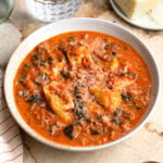 A shallow bowl of sausage tortellini soup with spinach topped with cheese