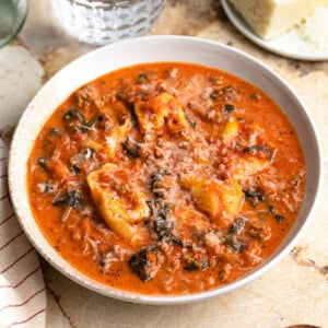 A shallow bowl of sausage tortellini soup with spinach topped with cheese