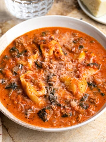 A shallow bowl of sausage tortellini soup with spinach topped with cheese
