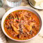 A shallow bowl of sausage tortellini soup with spinach topped with cheese
