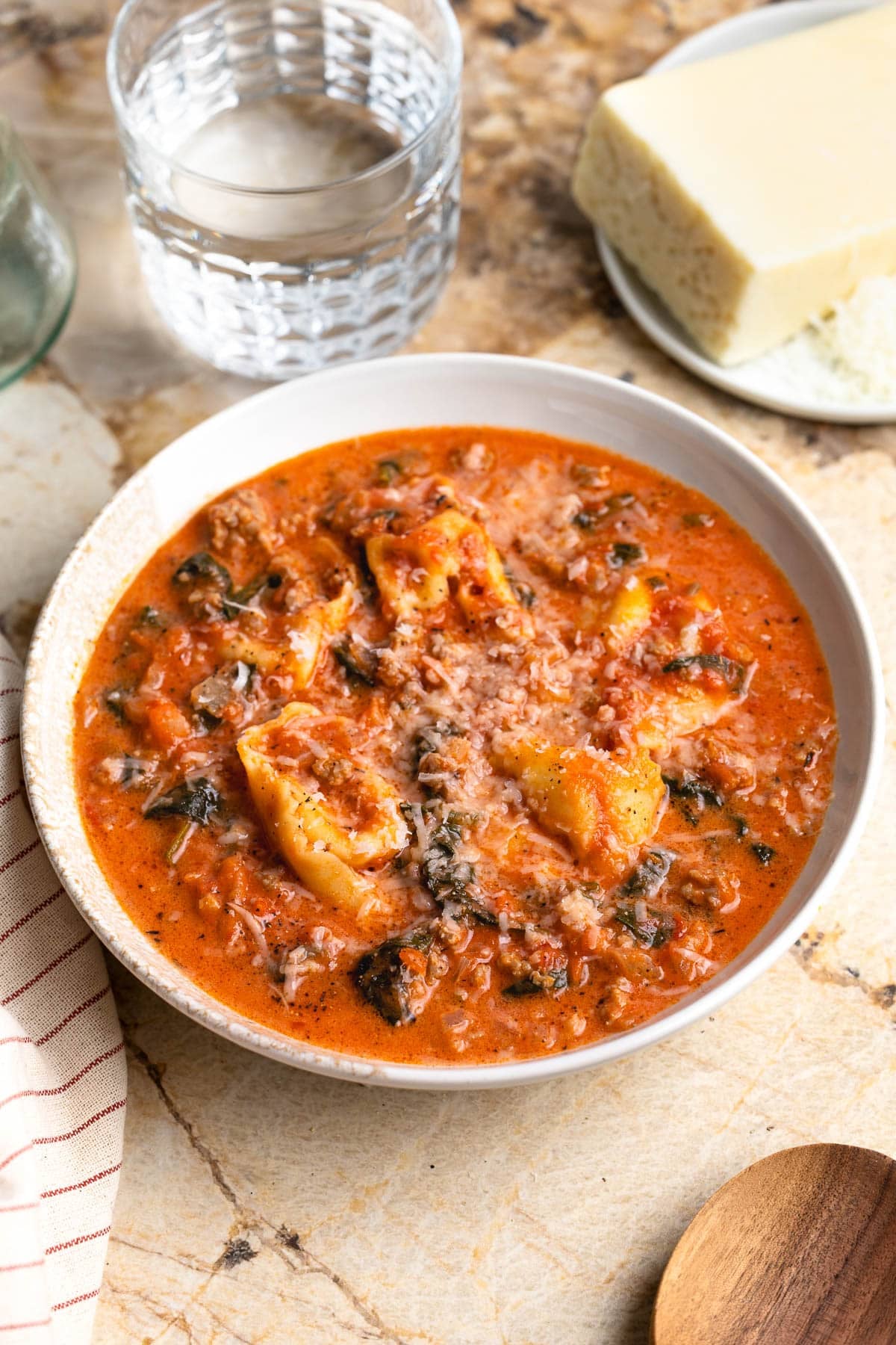 A shallow bowl of sausage tortellini soup with spinach topped with cheese