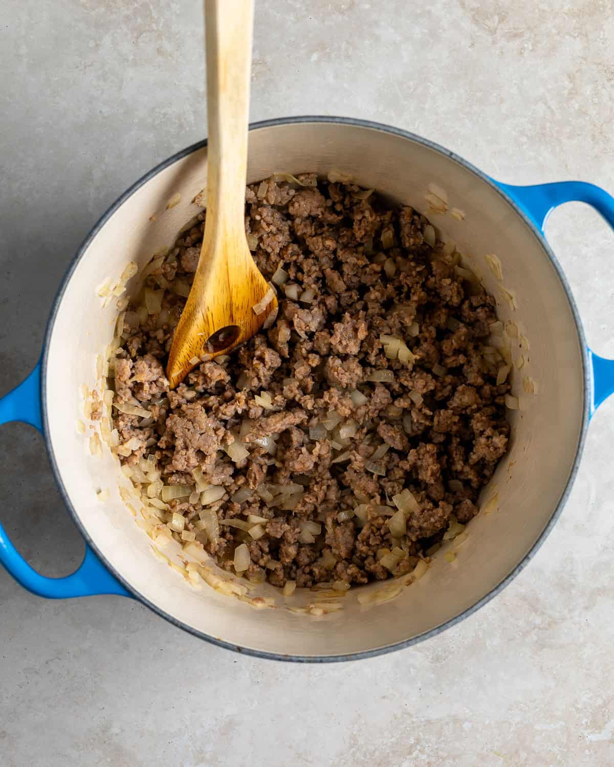 Crumbled sausage and onion in a pot.