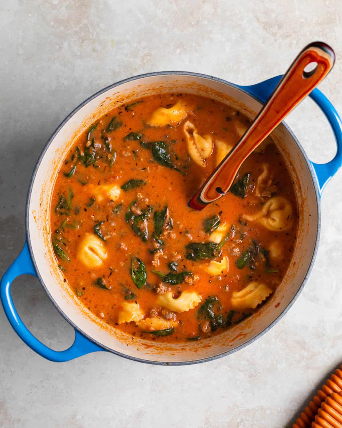 Cooked tortellini, cream, and wilted spinach in the pot of soup finishing it off.