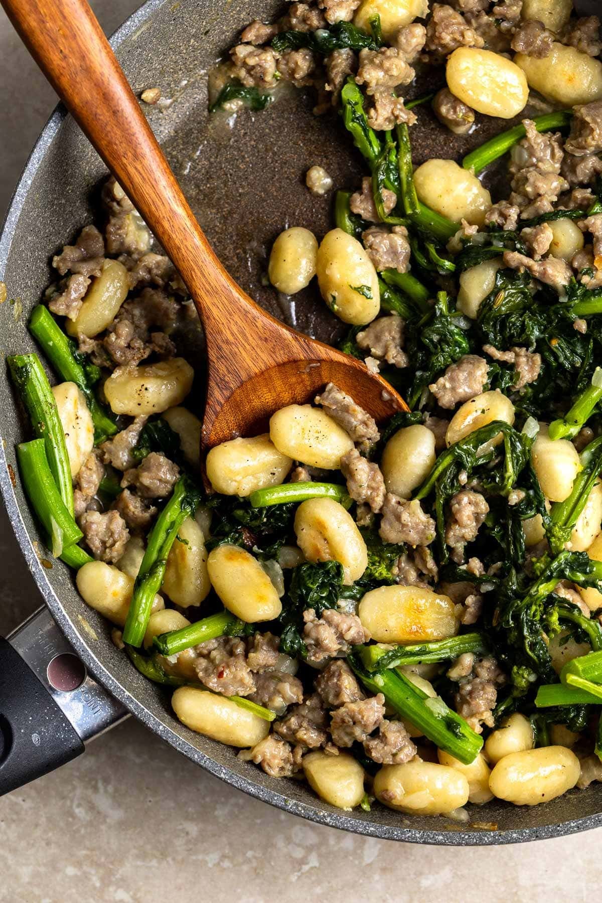 Skillet gnocchi, sausage, and broccoli rabe in a pan with a wooden serving spoon in it.
