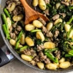 Skillet gnocchi, sausage, and broccoli rabe in a pan with a wooden serving spoon in it.