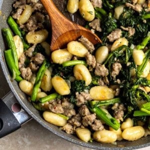 Skillet gnocchi, sausage, and broccoli rabe in a pan with a wooden serving spoon in it.