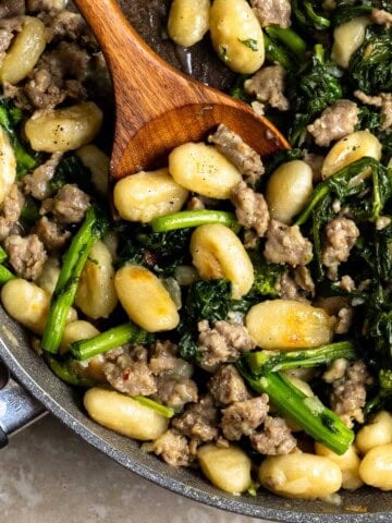 Skillet gnocchi, sausage, and broccoli rabe in a pan with a wooden serving spoon in it.