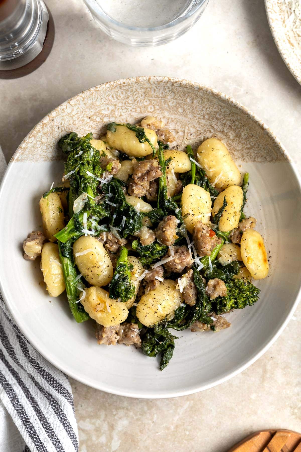 A serving of gnocchi, sausage, and broccoli rabe in a shallow bowl garnished with Pecorino.
