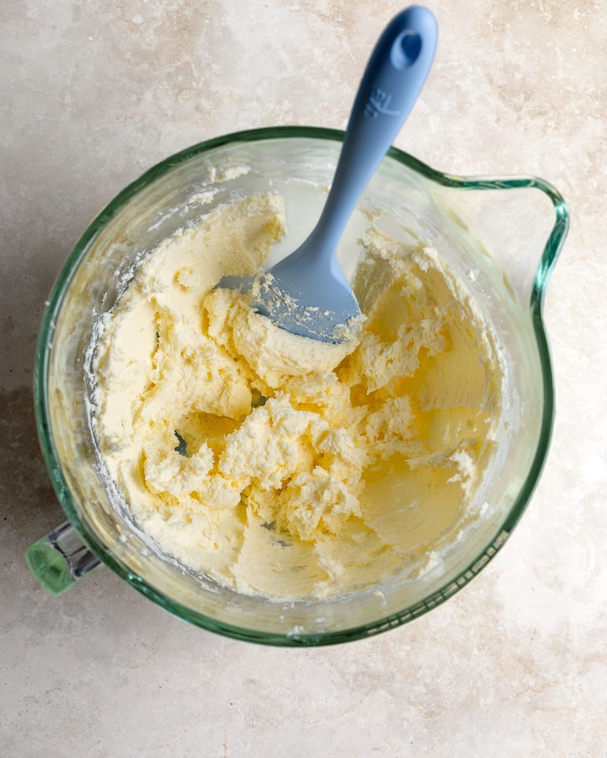 Creamed butter and cream cheese in a glass mixing bowl with a spatula.