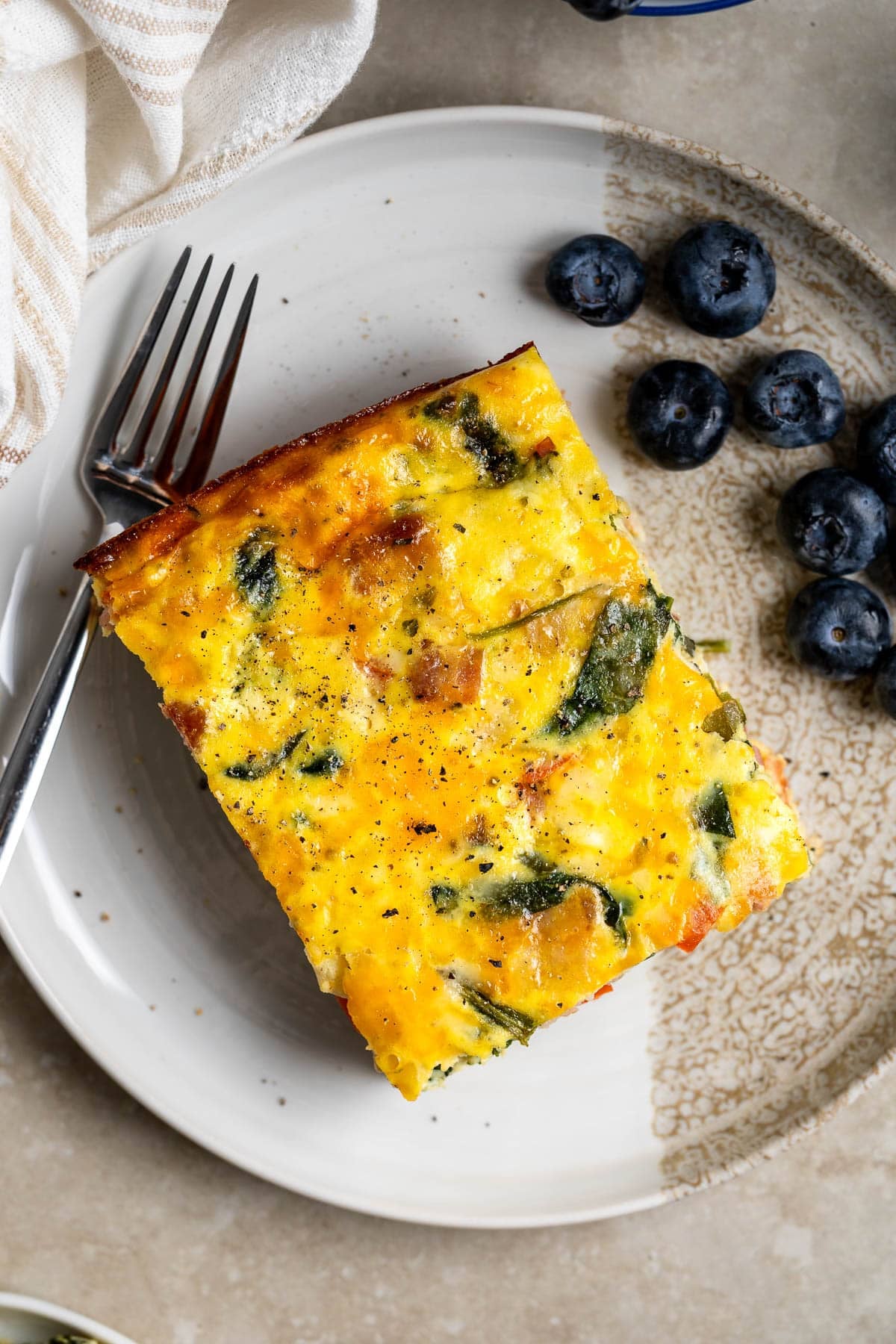 A square of egg bake on a plate with a fork and blueberries.