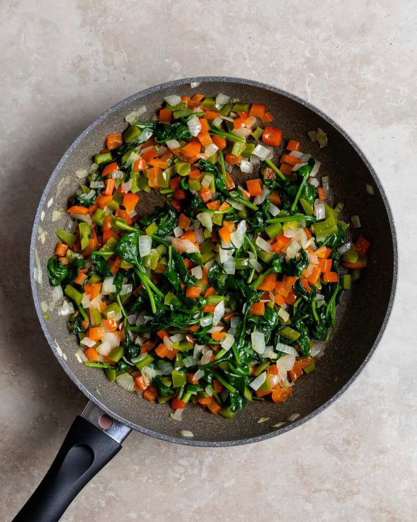 Sautéed peppers, onions, and wilted spinach in a pan.